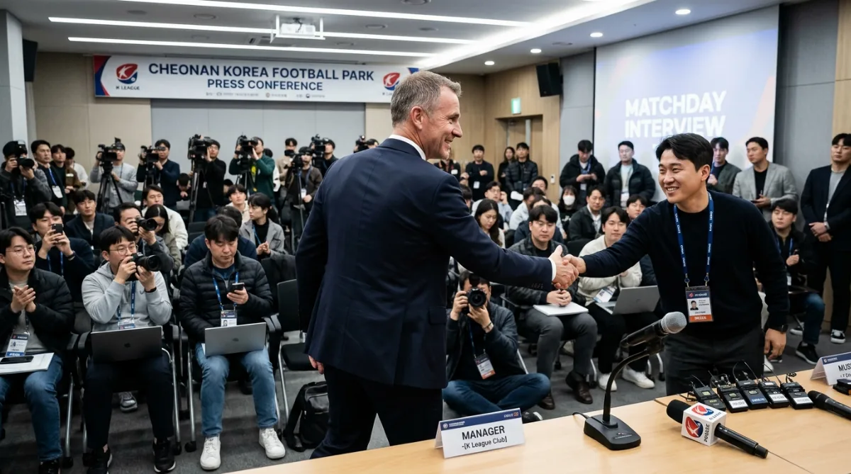 천안 코리아풋볼파크 회견장에서 정장 차림의 외국인 감독이 뒤돌아 서서 취재진과 악수를 나누는 원거리 구도